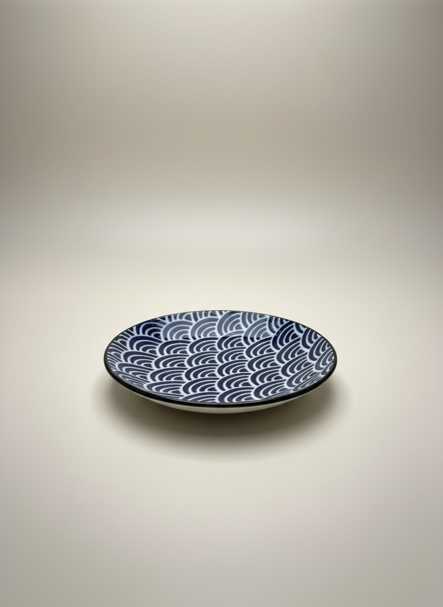 Assiette japonaise artisanale avec motif seigaiha vagues bleues concentriques sur fond blanc, extérieur noir profond céramique bicolore
